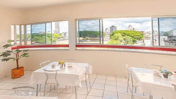 A hotel room with a tiled floor, a large window with a city view, and a potted plant. - Hotel Beira Rio (Itabuna)