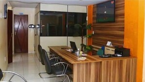 A reception desk with a wooden finish, black chairs, and a television mounted on the wall. - Hotel Beira Rio (Itabuna)
