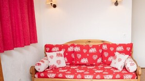 A wooden sofa bed with a red and white patterned cover, two wall-mounted lamps, and a red curtain. - 3-Room 6-Person Apt with Balcony in Puy-Saint-Vincent (Puy-Saint-Vincent)
