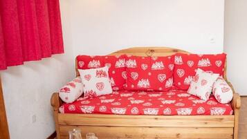 Un canapé-lit en bois recouvert d’un tissu à motifs rouges et blancs, deux lampes fixées au mur et un rideau rouge.