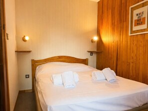 A neatly made bed with towels, wooden panel walls, and two wall-mounted light fixtures.