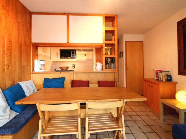 Una cocina compacta con microondas, cafetera y armarios de madera. Hay una mesa de comedor con dos sillas y un banco con cojines.