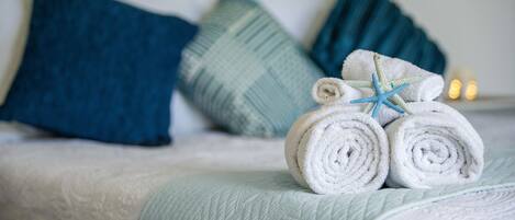 Un lit avec des serviettes blanches roulées et une étoile de mer bleue en guise de décoration.