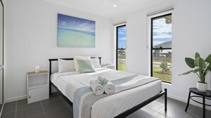 Une chambre à coucher moderne avec un grand lit, une table de chevet, une plante en pot et une vue sur l’extérieur.