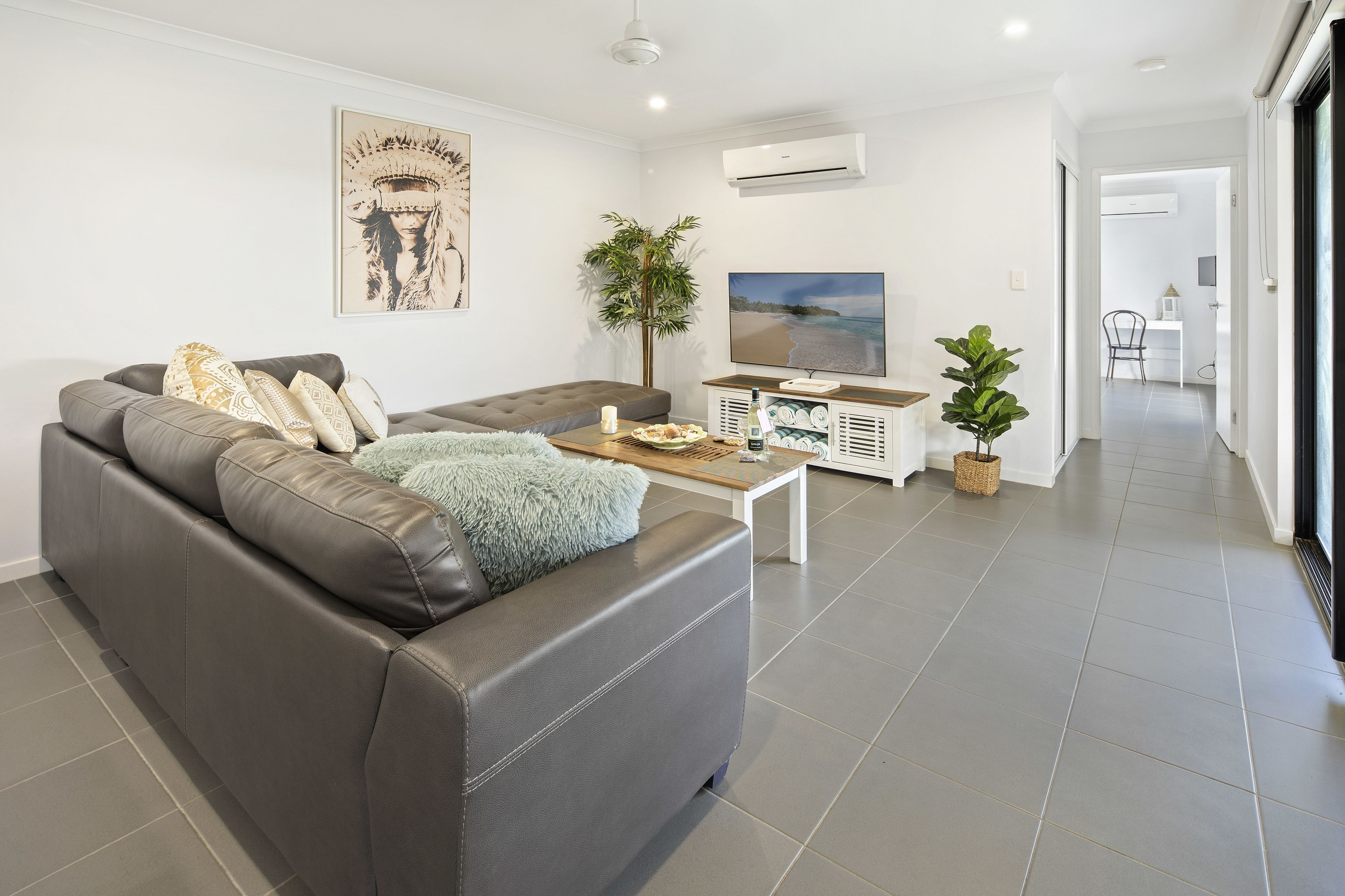 A modern living room with a grey leather sofa, a wooden coffee table, a flat-screen TV, and a potted plant.
