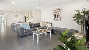 Un salon moderne avec un canapé d’angle gris, une table basse et une cuisine en arrière-plan.