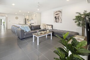 Una sala de estar moderna con un sofá seccional gris, una mesa de centro y una cocina al fondo.