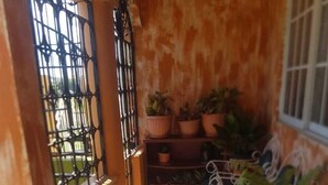 A small, sunlit room with a tiled floor, a metal gate, and several potted plants. - Victoria's Place (Portmore)