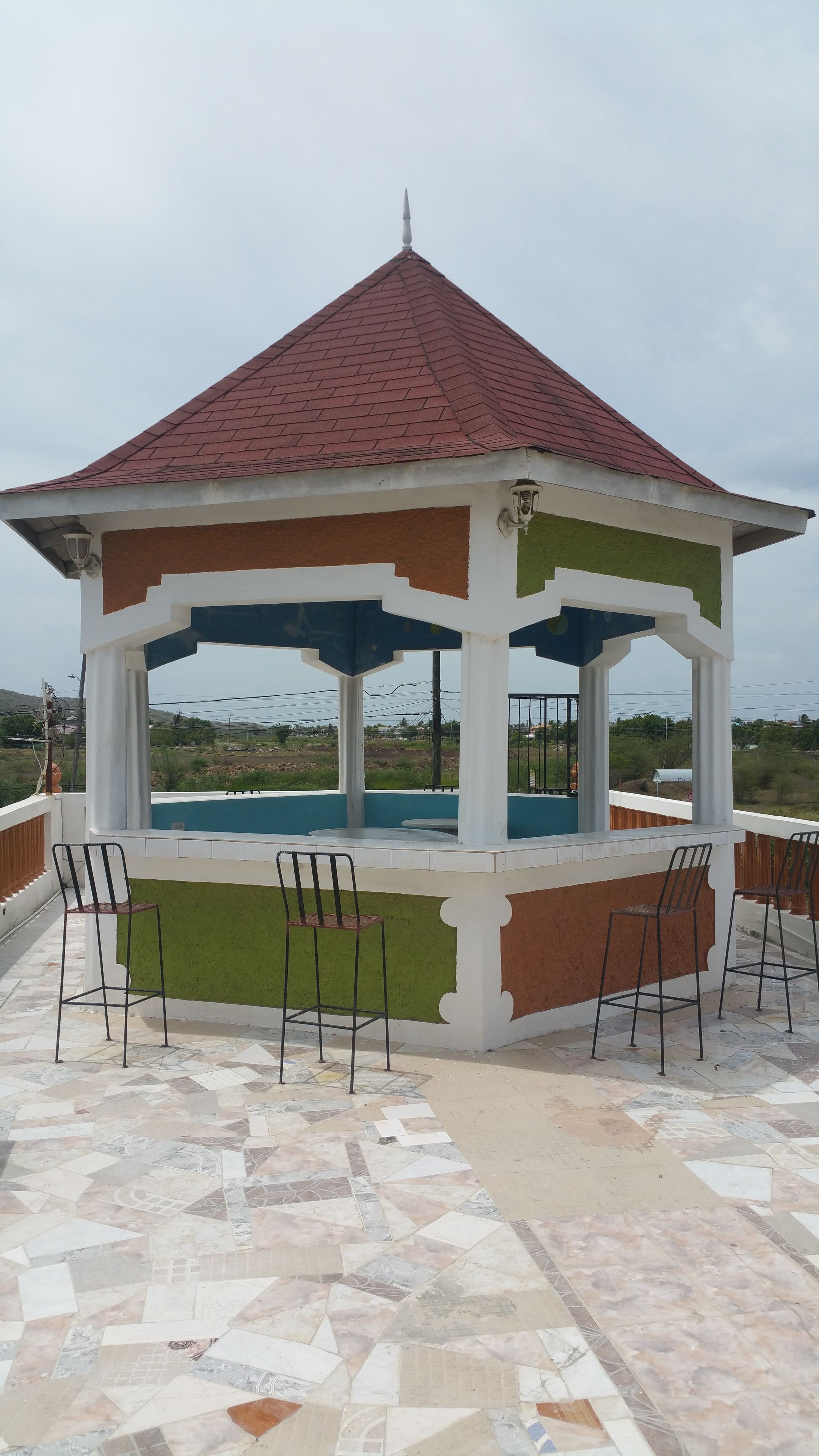 Un kiosque doté d’un sol carrelé et de chaises, donnant sur une piscine.