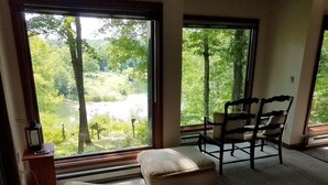 A room with a large window offering a view of a forested area and a body of water. There is a chair and a small ottoman in the room. - Scenic Setting Just 8 Minutes From Athens (Athens)