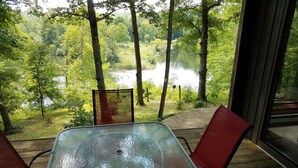 A glass-top table with two red chairs on a wooden deck overlooking a lake surrounded by trees. - Scenic Setting Just 8 Minutes From Athens (Athens)