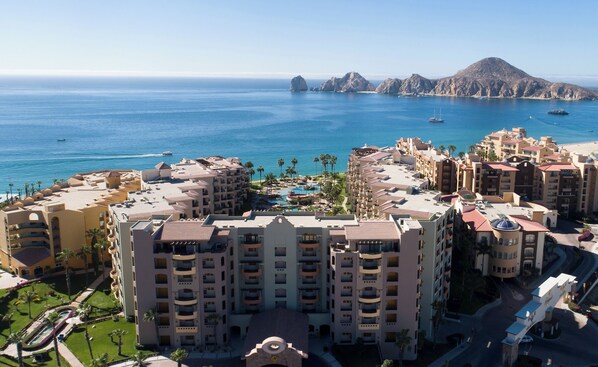 Un hotel costero con varias edificaciones, piscina y vista al mar y las montañas.