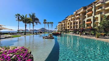 A resort pool with clear water, palm trees, and a view of the ocean.