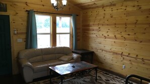 Una habitación acogedora con paredes de madera, un sofá color beige, una alfombra estampada y una mesita.