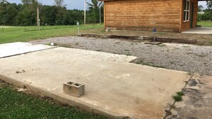 Una cabaña de madera con techo verde, un patio de concreto y una zona con grava.