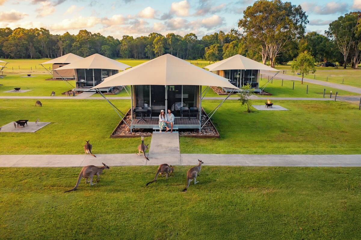 A series of modern, open-air structures with glass walls and flat roofs, surrounded by a well-maintained lawn and trees.