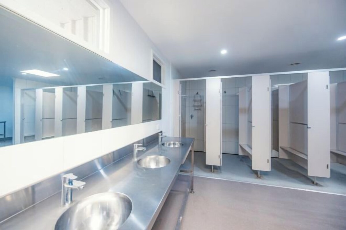 A modern bathroom with three sinks, a large mirror, and a row of lockers.