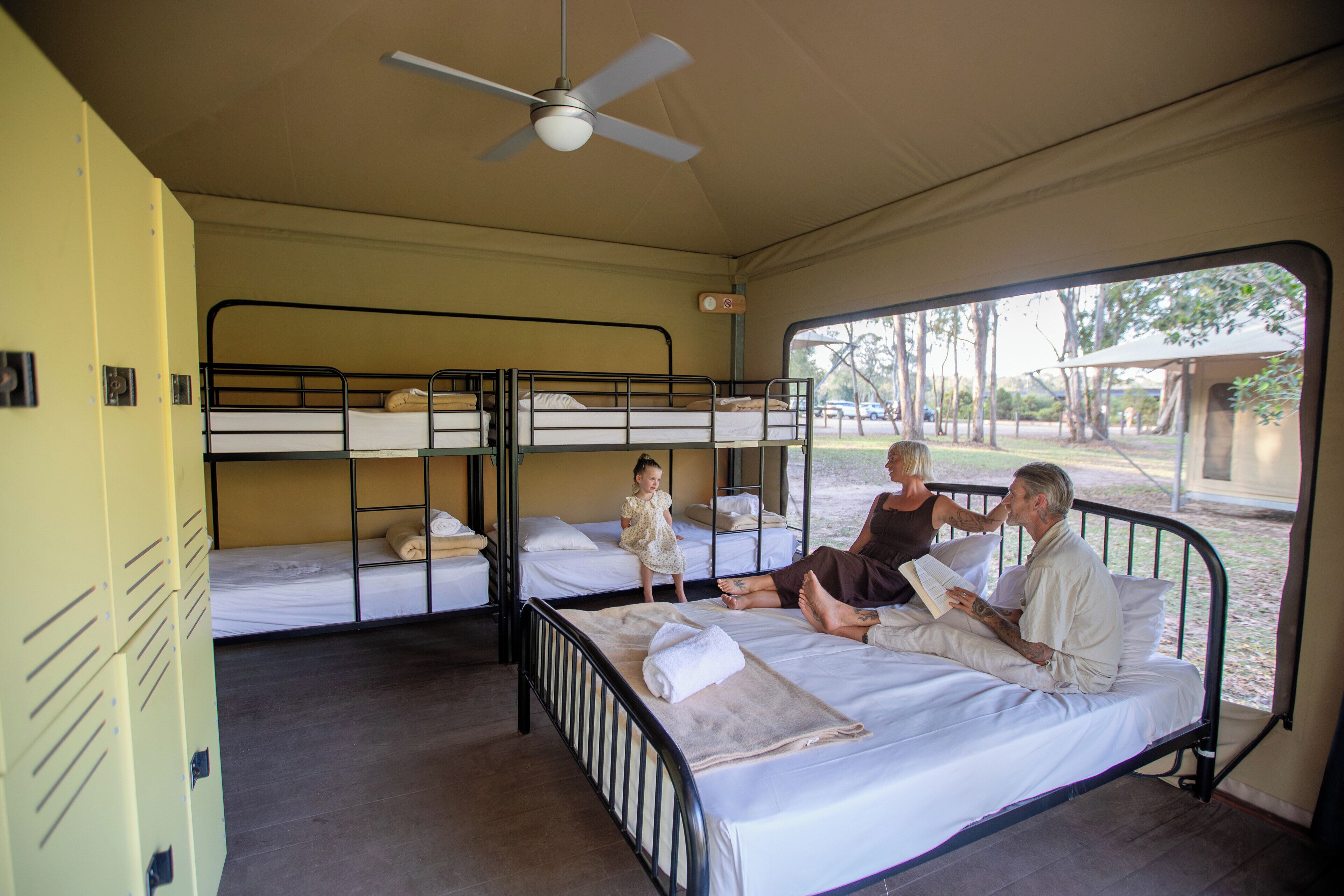 A room with bunk beds, a ceiling fan, and a window with a view of the outdoors.