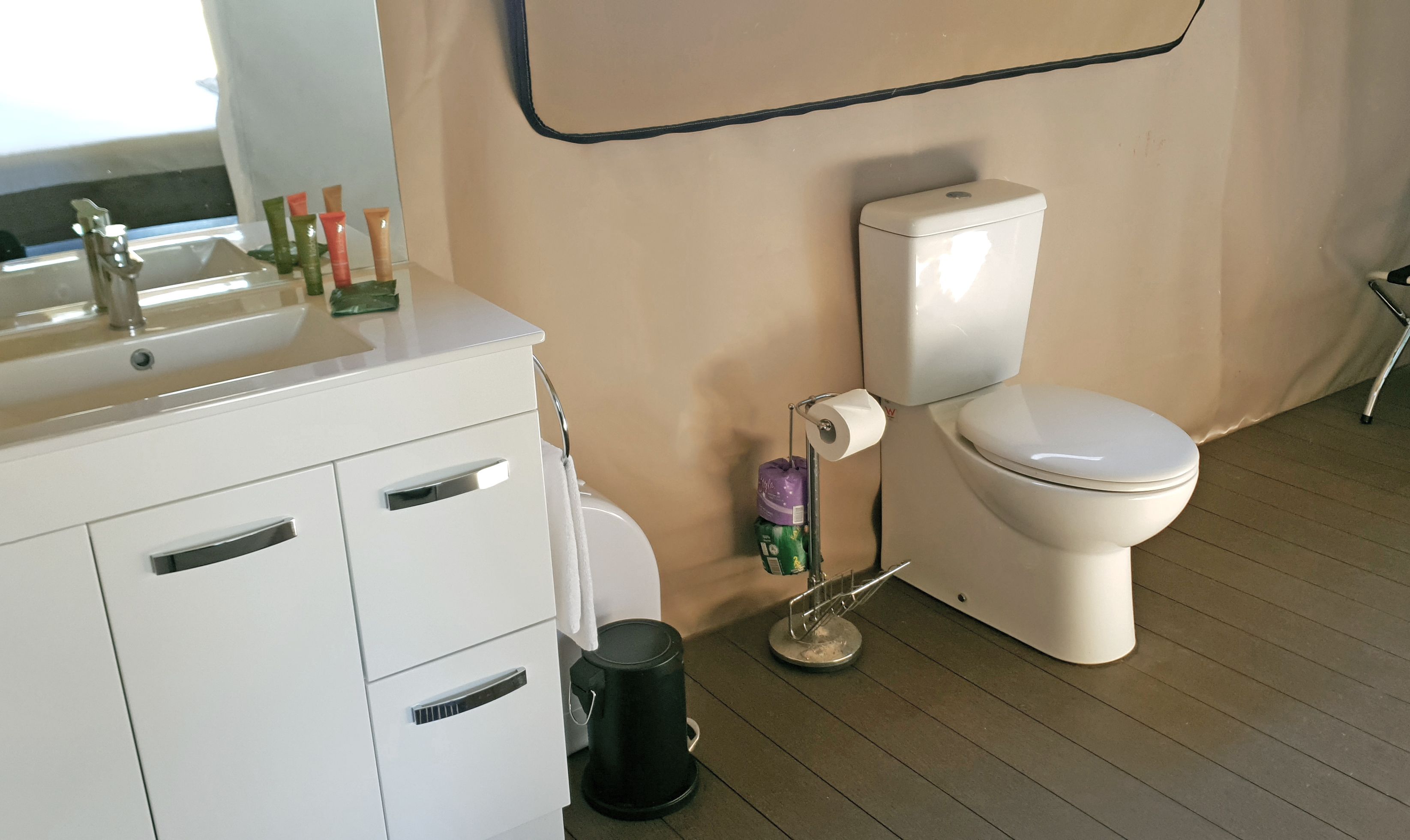A bathroom with a white sink, toiletries, a toilet, and a trash can.