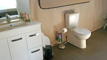 Un baño con lavamanos blanco, artículos de aseo, inodoro y cubo de basura.