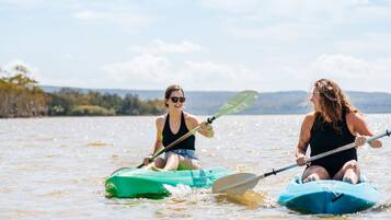 Dues persones fent caiac a un llac tranquil amb un cel serè i turons llunyans.