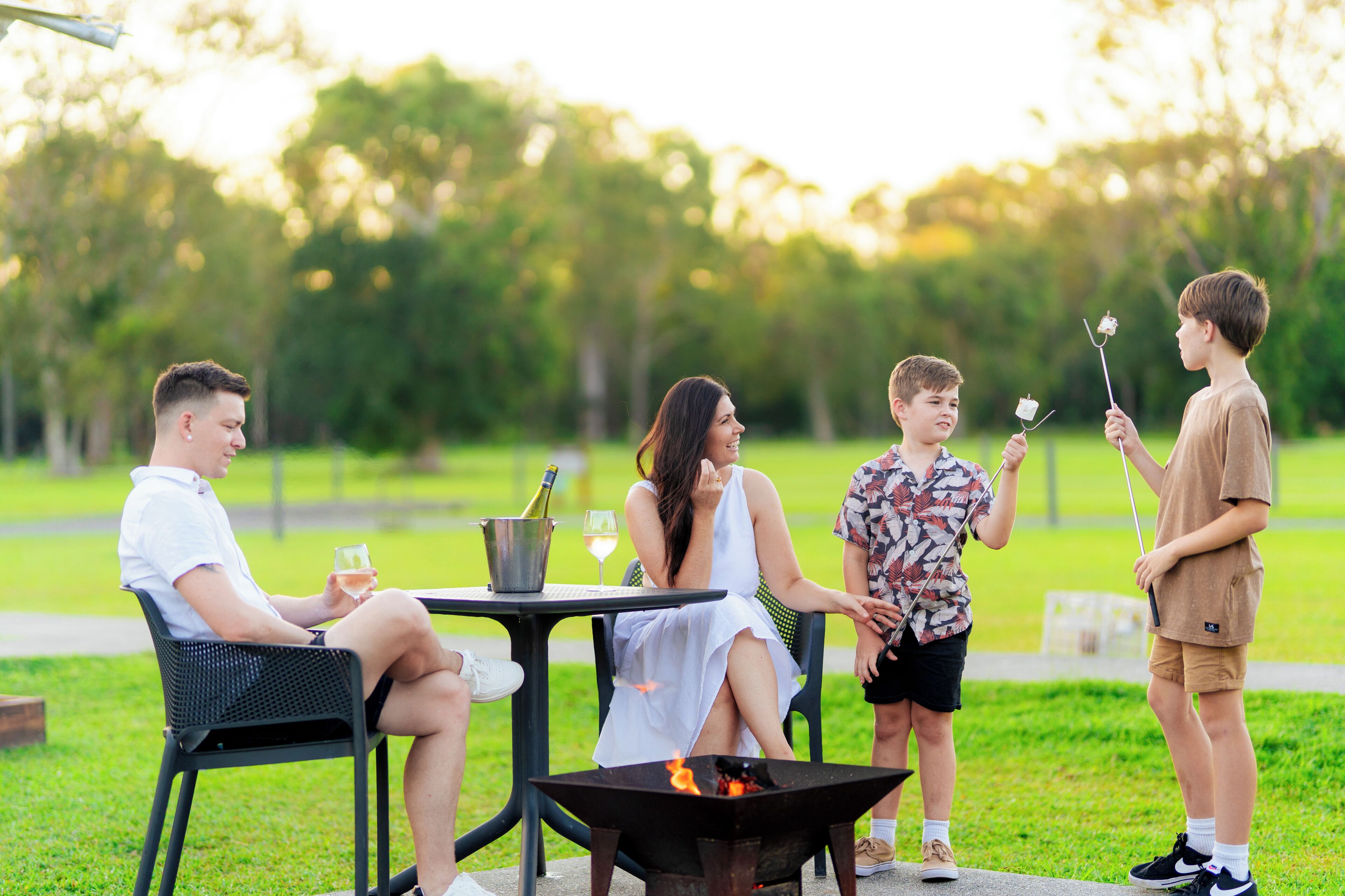 A group of people sitting around a table with a fire pit in the center.
