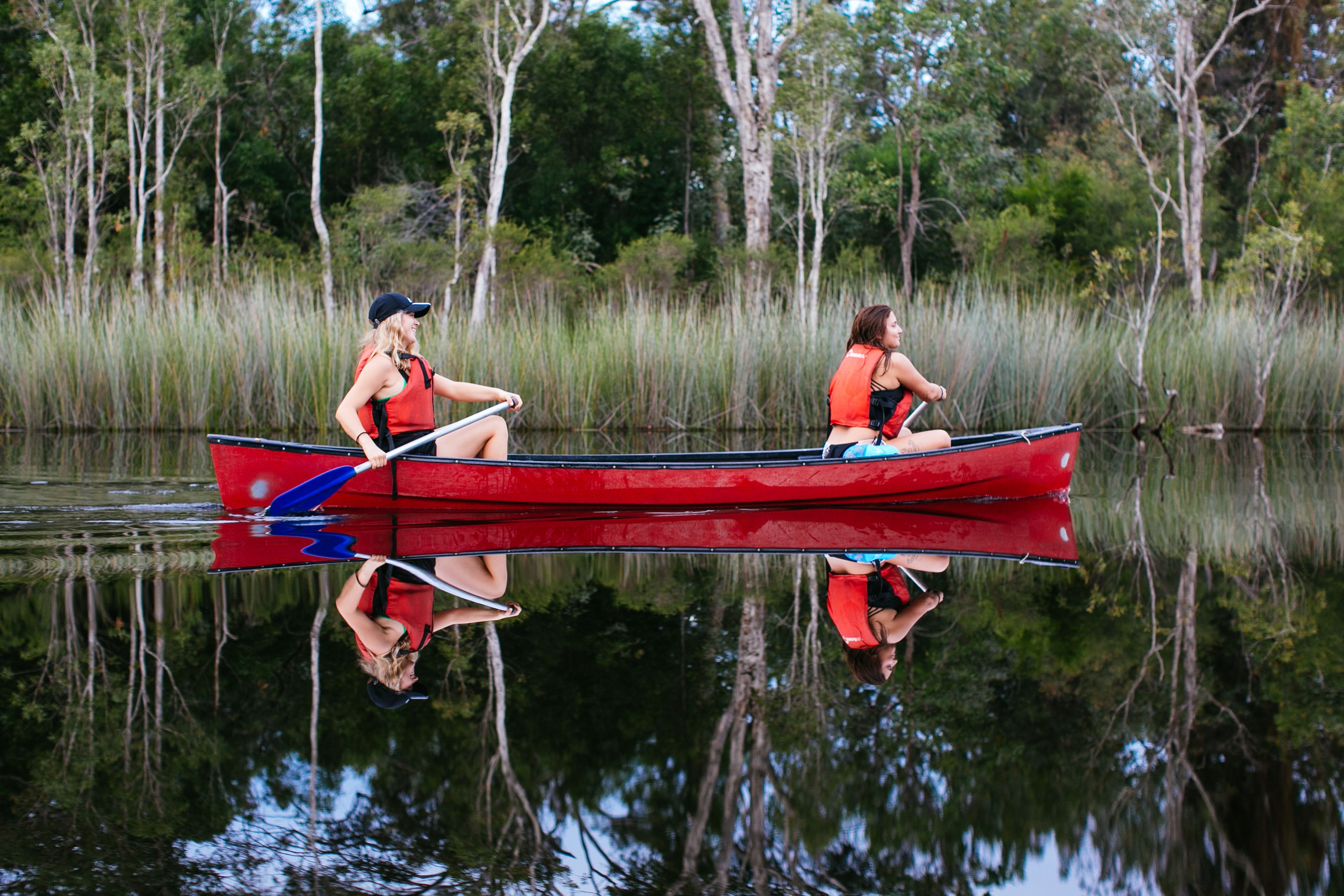 Dos personas en un canoa roja sobre aguas tranquilas, rodeadas de árboles.