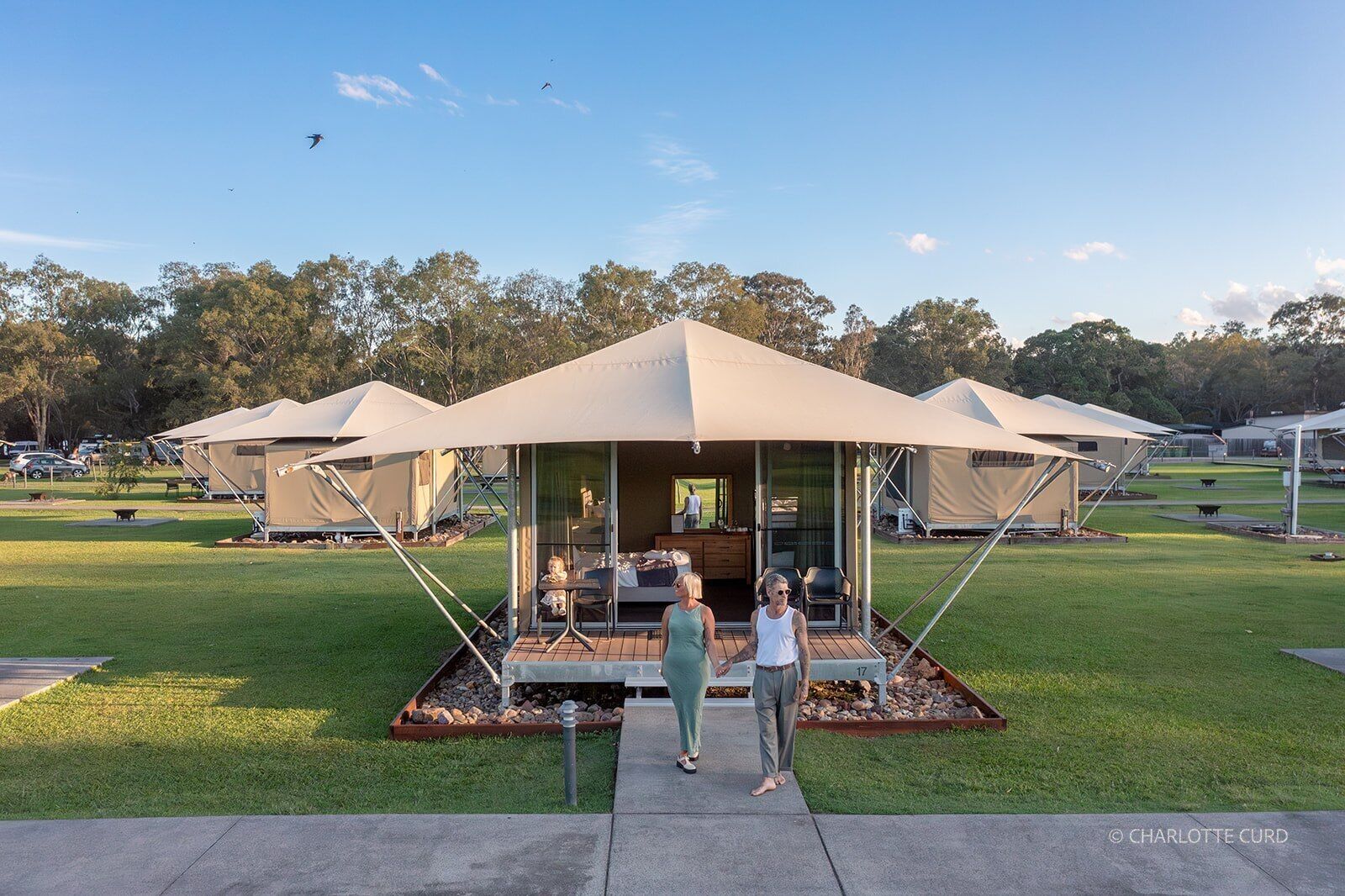 Una serie de estructuras modernas con forma de tienda, con puertas de cristal, ubicadas en un área verde con árboles al fondo.