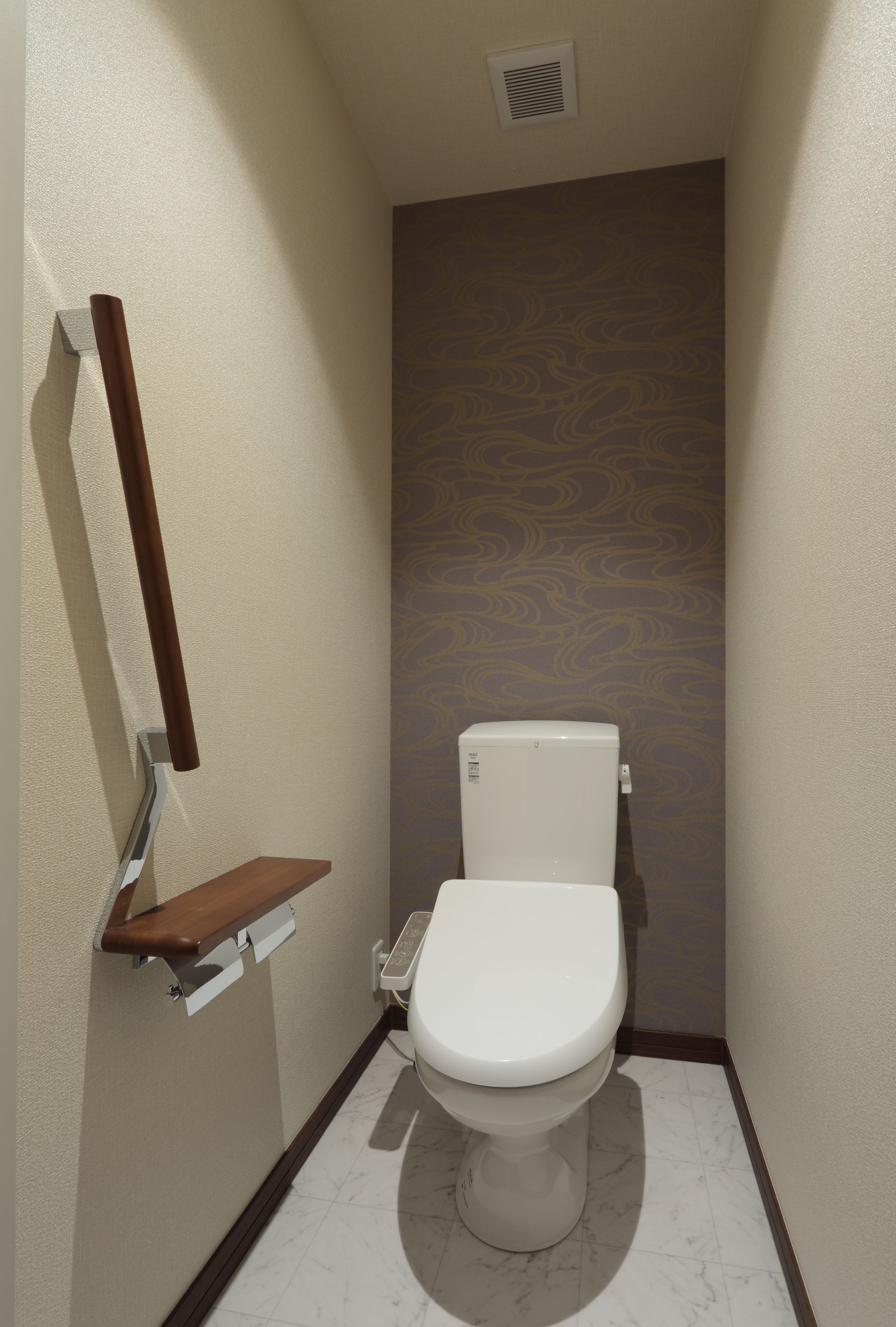 Une petite salle de bain étroite, avec des toilettes, une étagère en bois et un mur orné d’un motif.