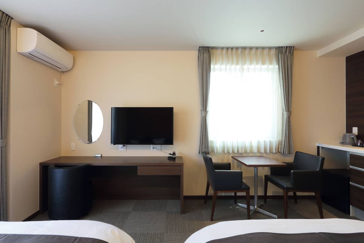 A hotel room with a bed, a desk with a chair, a television, a mirror, and a window with curtains.