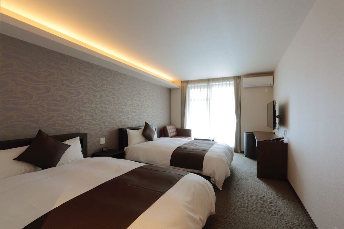 A hotel room with two beds, a flat-screen TV, and a large window with curtains.