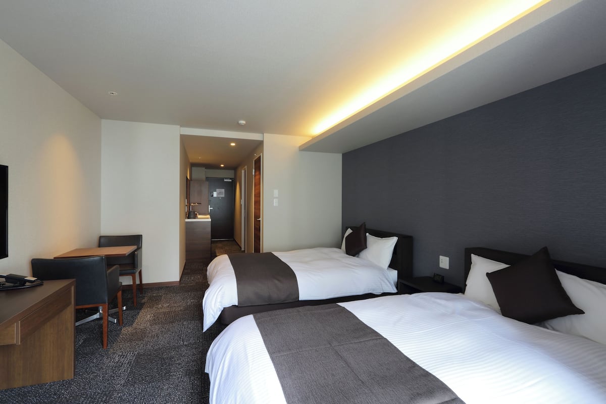 A hotel room with two beds, a desk, and a television.