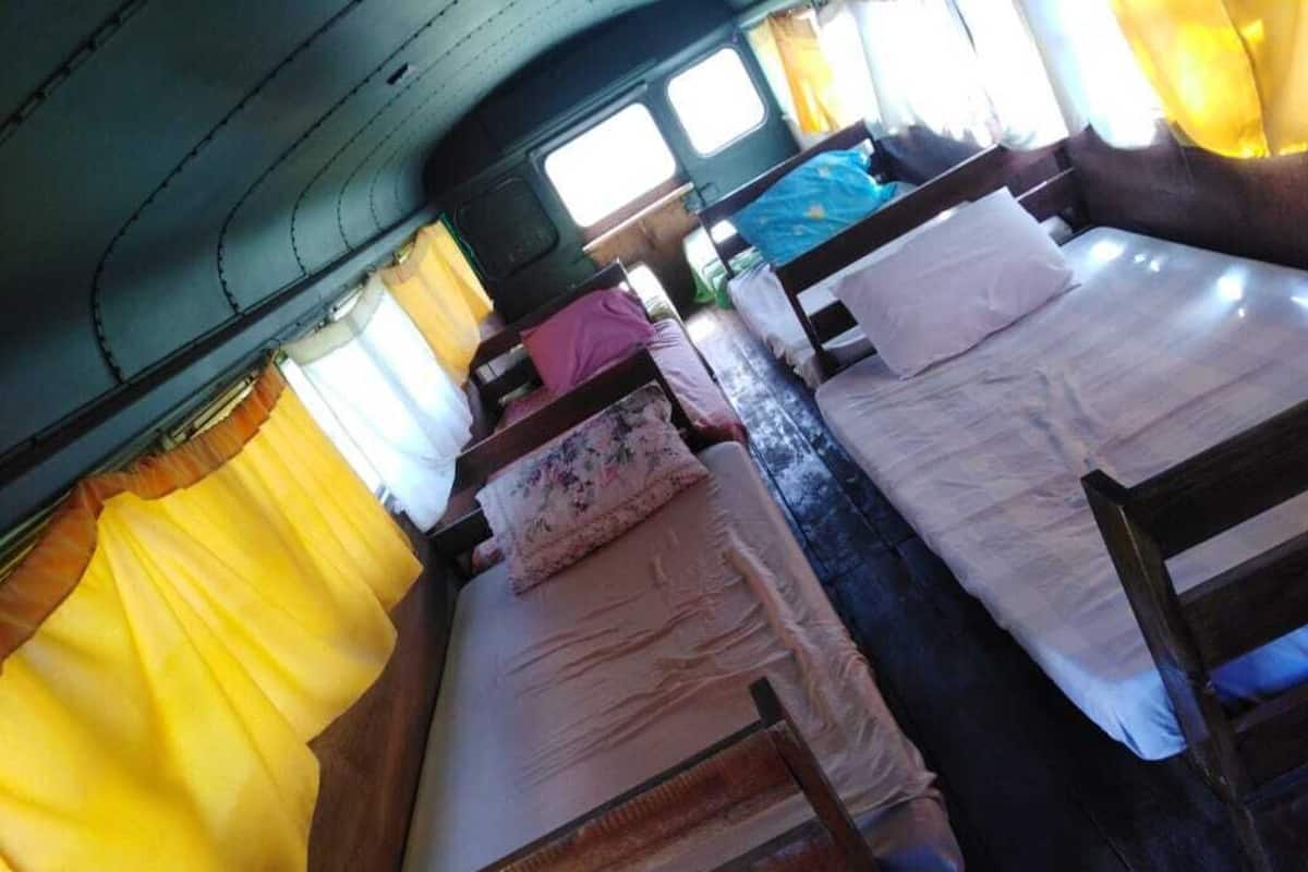 A compact room with two beds, each with a wooden frame and white bedding. There are curtains on the windows, and the room has a simple, functional design.
