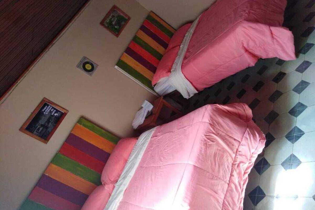 A room with two beds covered in pink bedding, a colorful striped wall hanging, and a framed picture on the wall.