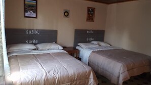 Two beds with headboards labeled 'Suena' in a room with a poster on the wall and a small table beside one bed. - Mitos Hostal (Intibucá)