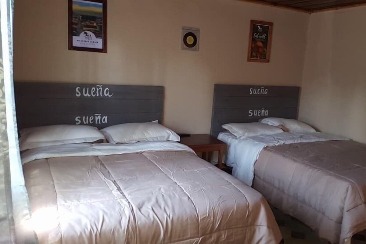 Dos camas con cabeceras etiquetadas 'Suena' en una habitación con un póster en la pared y una mesita de noche al lado de una cama.