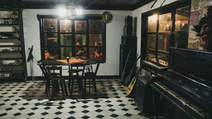 A room with a checkered floor, a piano, a table with chairs, and a window with reflections. - Mitos Hostal (Intibucá)