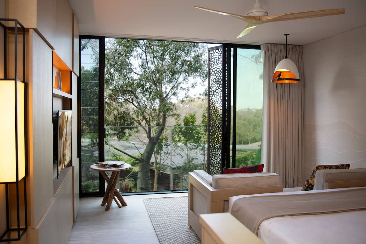 A modern hotel room with a large sliding glass door leading to a balcony, a ceiling fan, and a bed with a view of the outdoors.