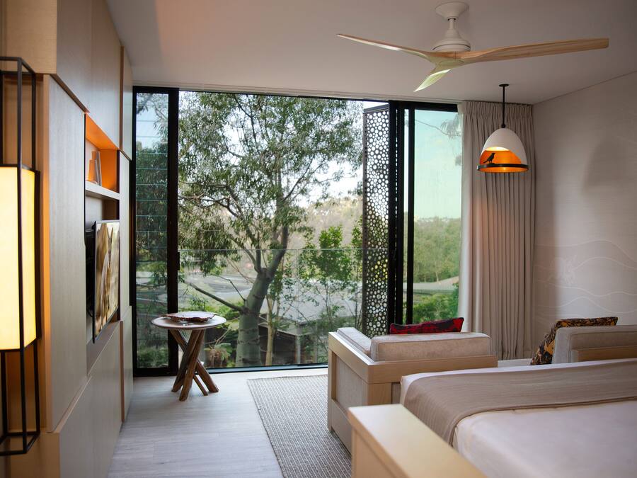 A modern hotel room with a large sliding glass door leading to a balcony, a ceiling fan, and a bed with a view of the outdoors.