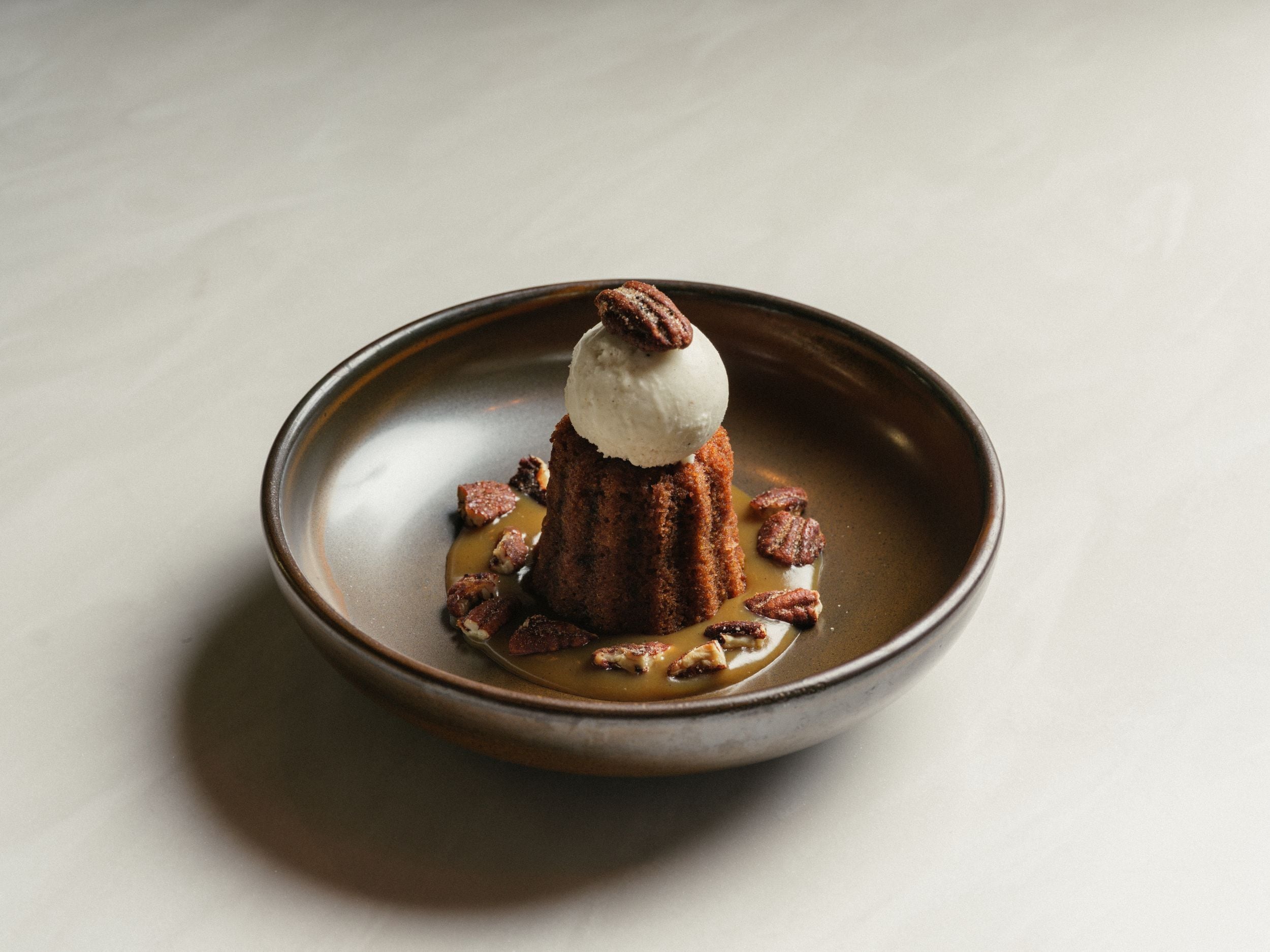 A dessert with a scoop of ice cream on top, surrounded by caramel sauce and pecans, served in a ceramic dish.