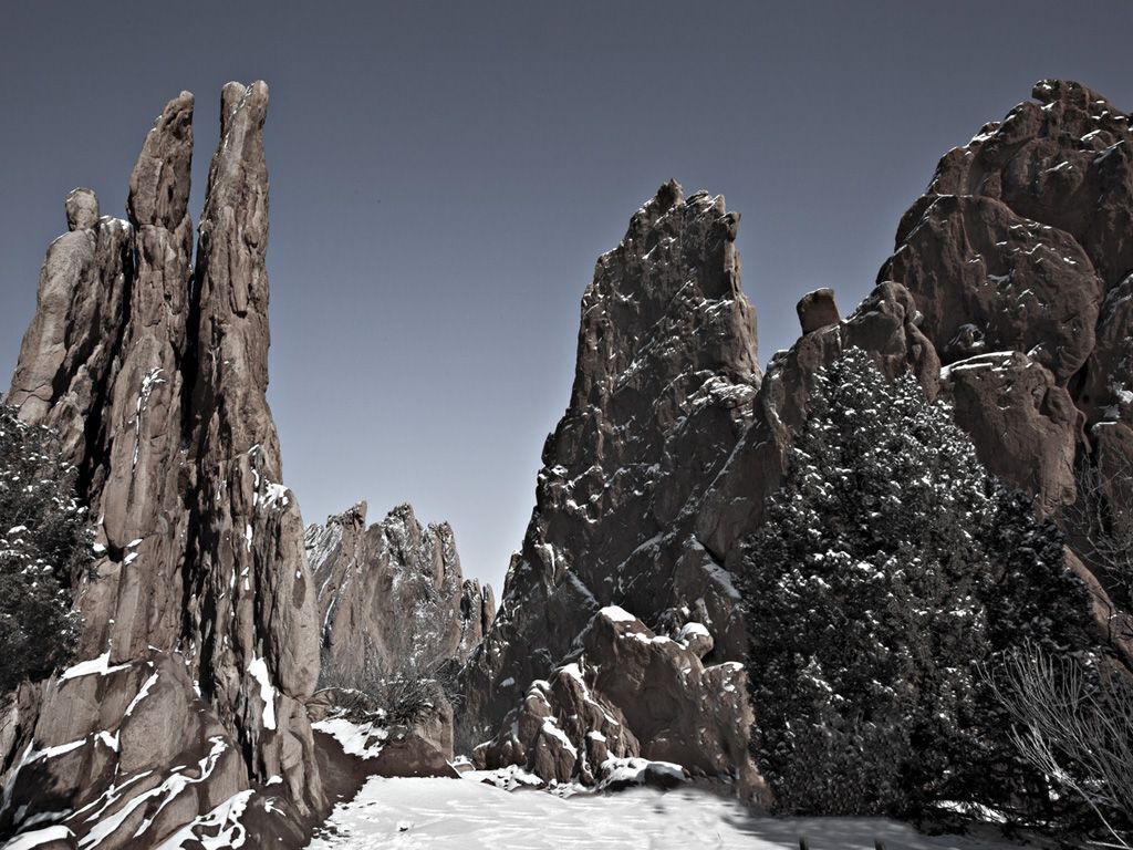 A rugged mountainous landscape with snow-covered rock formations and sparse vegetation.