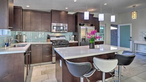 Una cocina moderna con armarios de madera oscura, electrodomésticos de acero inoxidable, una isla grande con taburetes altos e iluminación colgante.