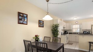 A dining area with a table and chairs, a hanging light fixture, and a kitchen with cabinets and appliances. - Minium At Lakeside Golf & Cc - Unit 104 3 Bedroom Apts by RedAwning (Inverness)