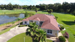 A single-story house with a red roof, surrounded by a well-maintained lawn and a small pond. - Spacious Modern Pool Home, Family & Golf Trips - 4727 4 Bedroom Home by RedAwning (Inverness)
