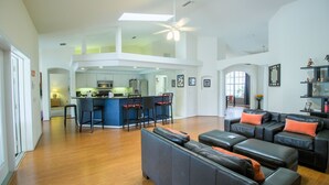 A spacious living area with a high ceiling, a central kitchen, and a seating area with a sofa and ottoman. - Spacious Modern Pool Home, Family & Golf Trips - 4727 4 Bedroom Home by RedAwning (Inverness)