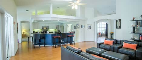 A spacious living area with a high ceiling, a central kitchen, and a seating area with a sofa and ottoman.