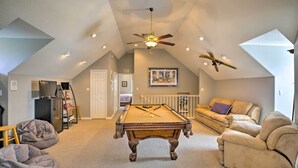 A spacious living room with a pool table, a ceiling fan, and a large window. - Waterfront Lake Placid Home w/ Dock & Fire Pit (Lake Placid)