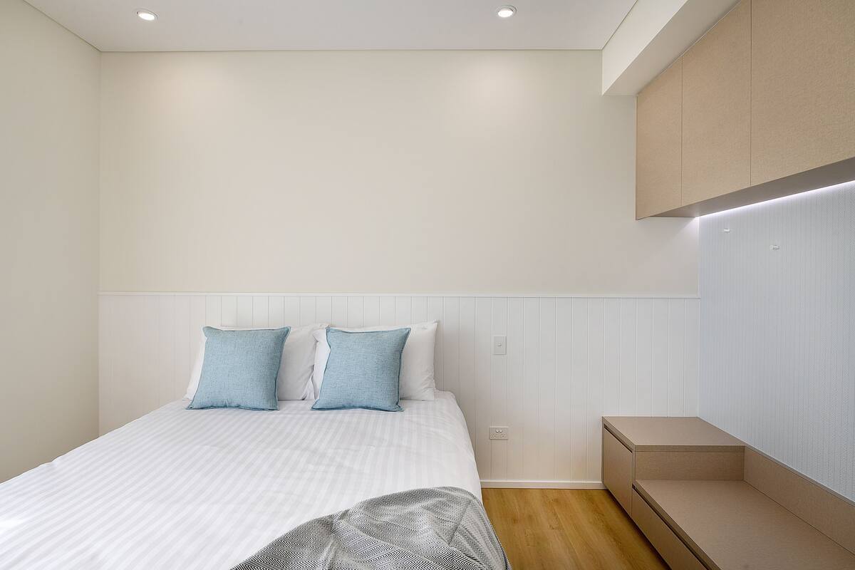 A bedroom with a bed, two pillows, a bedside table, and a built-in bench.