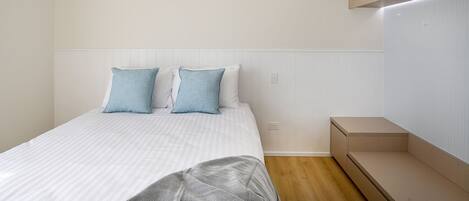 A bedroom with a bed, two pillows, a bedside table, and a built-in bench.