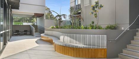 A modern outdoor seating area with a curved wooden bench and a built-in cushioned bench, surrounded by plants and a staircase.